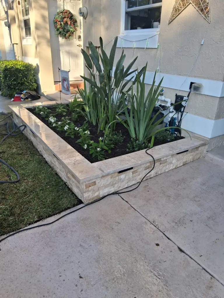 Square stone veneer planter bed beside a front entry walkway