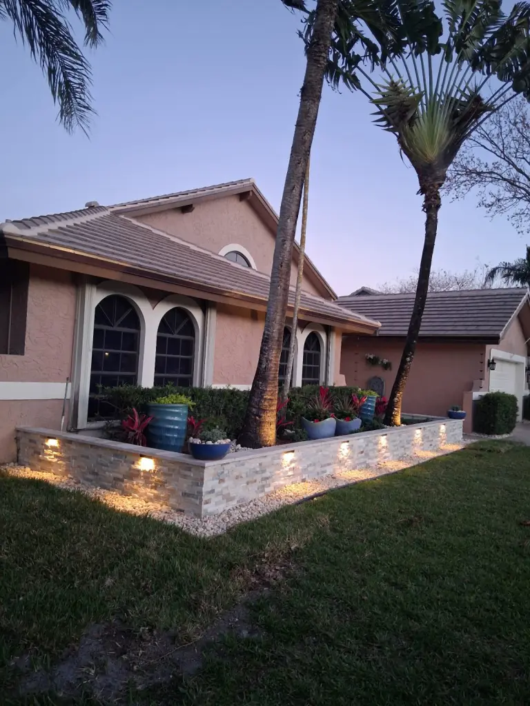 Raised front-yard border lit at dusk beneath two palm trees
