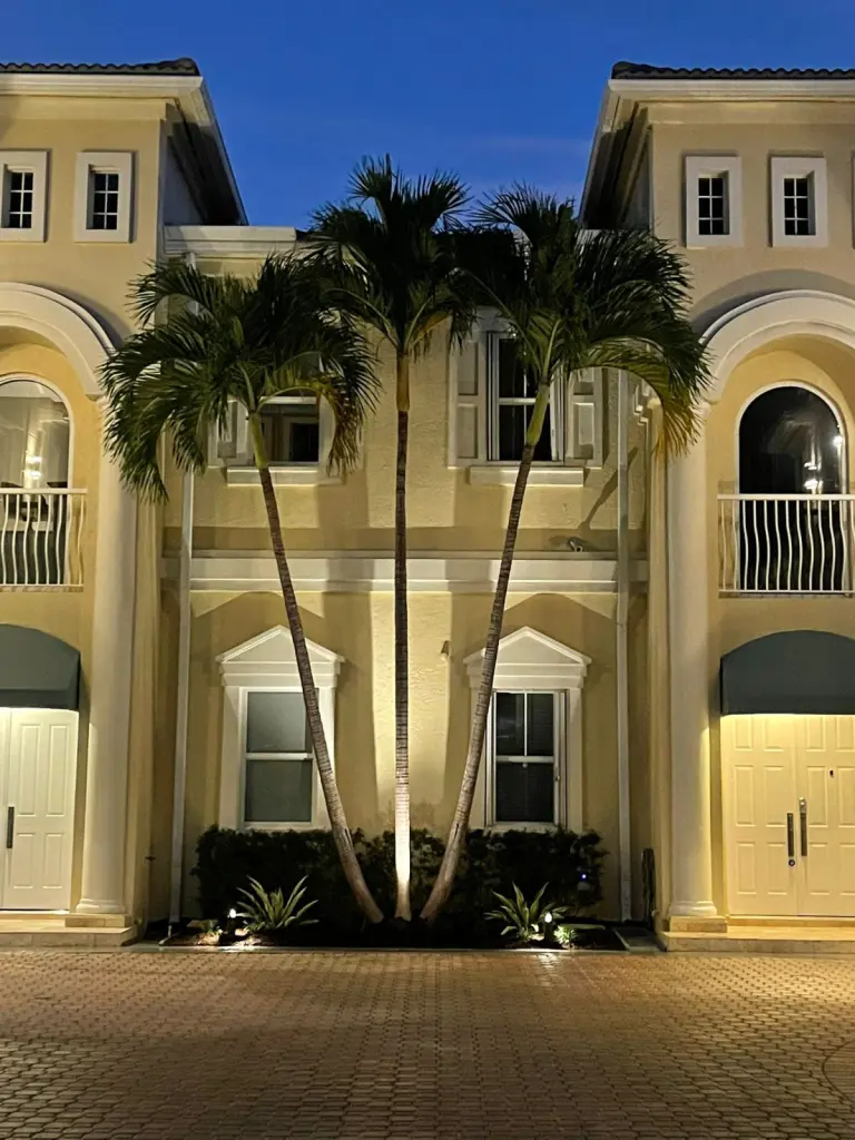 Palm trees uplit at night in front of a two-story home entrance