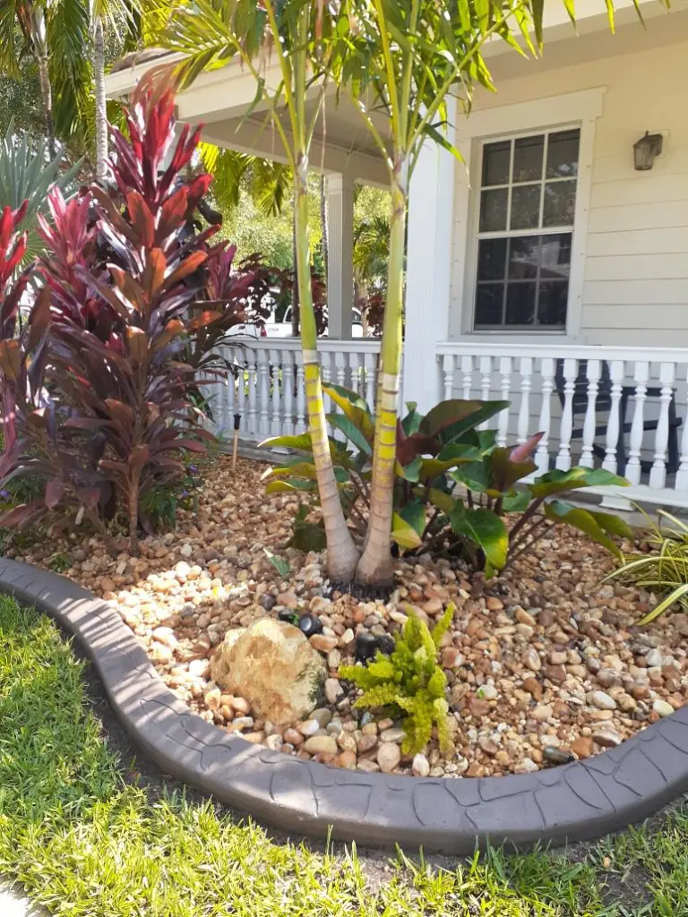 Grey curved concrete border around red ti plants by a porch