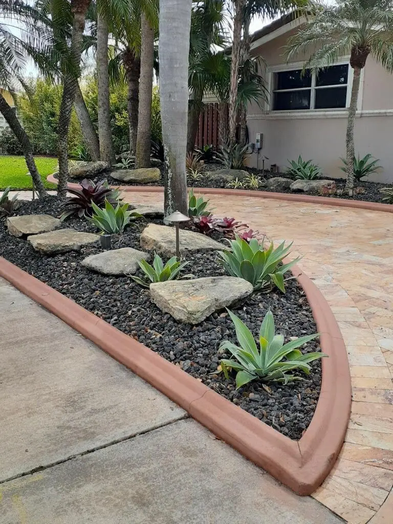 Terracotta-colored border separating a boulder bed from a paver driveway