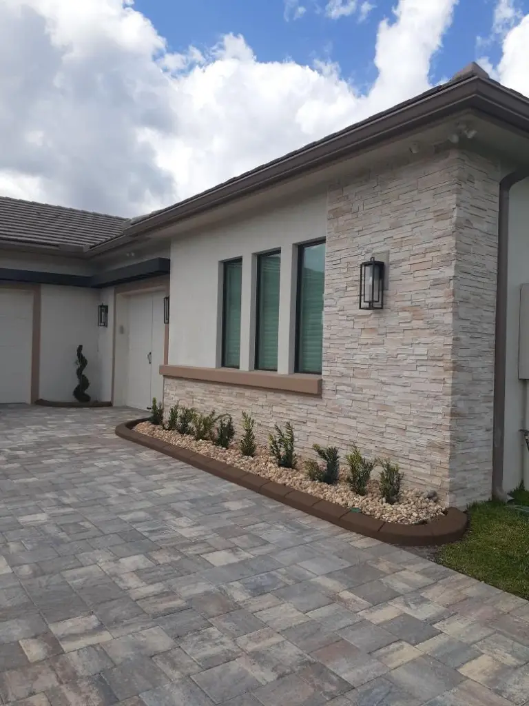 Grey paver driveway beside a stone-clad house with a planting strip