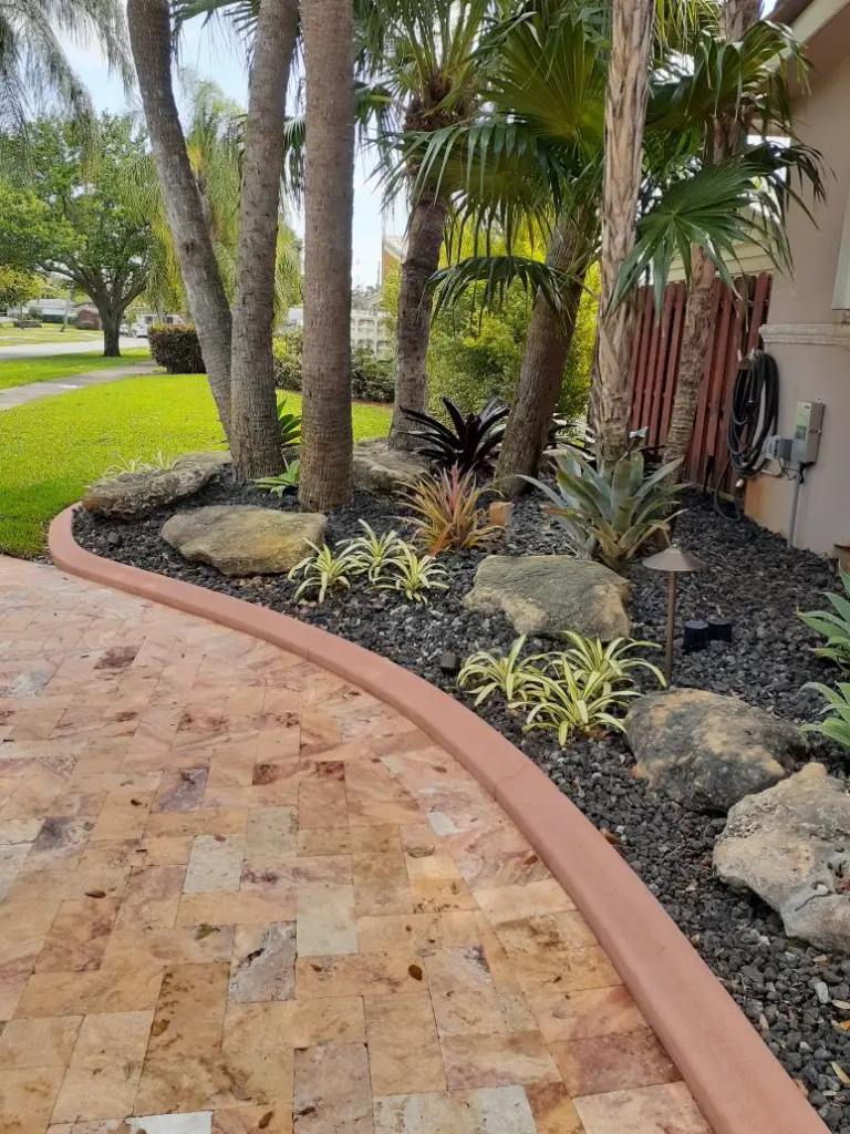 Tan paver walkway edged by a curved border and rock bed